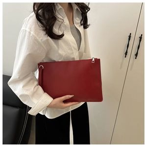 Close-up of a red leather envelope clutch with silver zipper and wristlet strap on a model