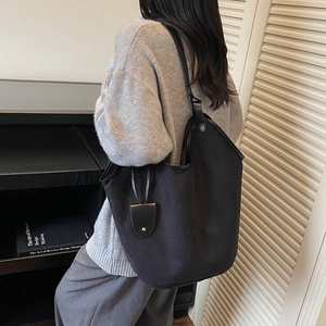 Minimalist black tote bag with suede texture and leather trim worn on shoulder