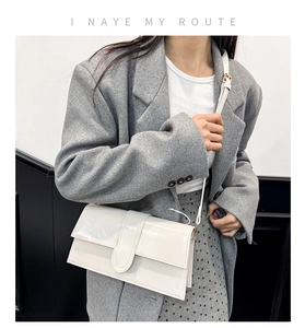 Fashionable cream white glossy leather envelope crossbody bag worn over a grey blazer