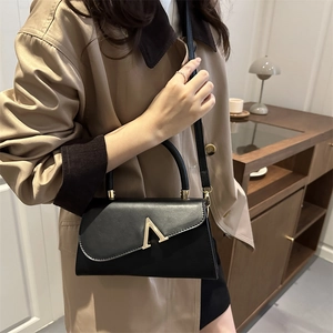 Elegant black leather handbag with gold V-buckle accent and shoulder strap worn with coat