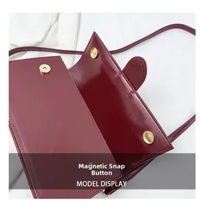 Detail view of the secure magnetic button closure on the burgundy faux leather baguette bag