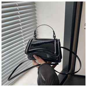 Detail of a black glossy patent leather mini crossbody bag held by a person