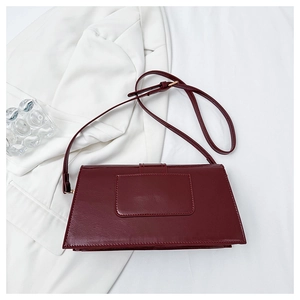 Close-up of wine red rectangular shoulder bag on white fabric with textured glass