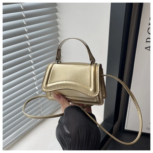Detail of a structured gold crossbody bag with a wave pattern flap and sleek metal handle