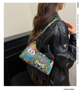 Close-up of vibrant multi-colored snakeskin crossbody bag on a black leather jacket