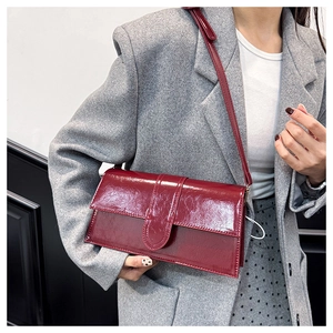 Detail of burgundy glossy leather baguette bag worn with a gray wool blazer