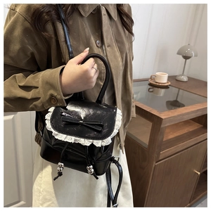 Detail of a black mini backpack featuring white lace trim and a bow on glossy leather