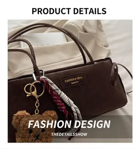 Close-up of brown suede underarm bag with teddy bear charm and brand logo tag