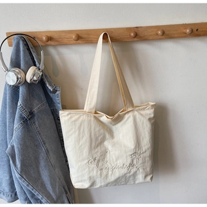 Détail de broderie de fleurs et cœurs sur le sac cabas en toile blanc cassé