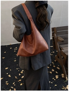 Detail of dark brown leather tote bag with embossed lettering on model in gray blazer