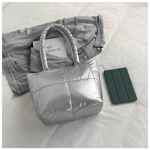 Detail of silver metallic quilted puffer bag with soft padded handle on white linens