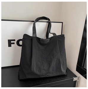 Detail of black tote bag with textured fabric, leather handles and embossed brand logo