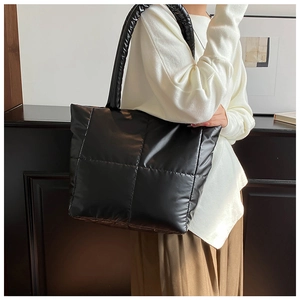 Detail of a black quilted puffer tote bag with glossy finish and wide soft shoulder strap
