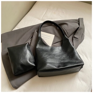 Detail of black matte leather hobo bag set with matching pouch on grey fabric background