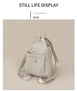 Detail of beige nylon backpack with drawstring closure and metal M logo on desk