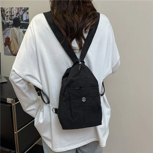 Minimalist black nylon backpack featuring a front pocket and circular metallic M logo