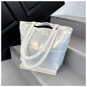 Detail of silver quilted puffer tote bag with metallic finish resting on a grey staircase