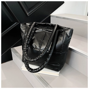 Detailed macro view of black quilted down tote bag with pleated handles and glossy texture