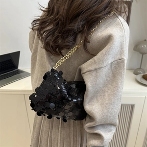 Chic black sequin crossbody bag with gold chain strap shown on a model in a minimal setting