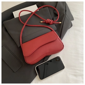 Macro shot of red curved flap bag with braided strap on a grey blazer for size reference