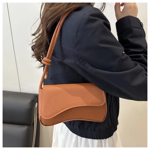 Detail of brown leather baguette bag with knotted shoulder strap and textured finish