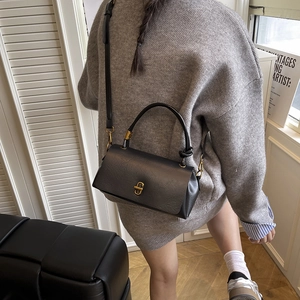 Classic black square handbag with gold metal lock and leather texture in a modern room