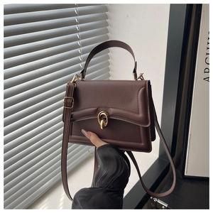 Detail of the golden twist-lock closure on a dark brown matte leather handbag