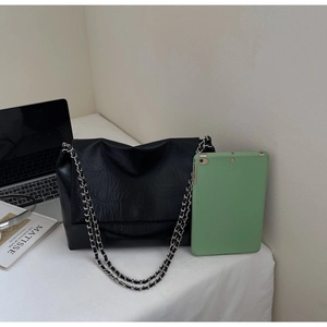 Detail of black wrinkled leather shoulder bag with silver dual chain straps on a white desk