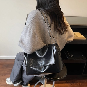 Glossy black pleated chain underarm tote bag worn by a model in a minimalist room
