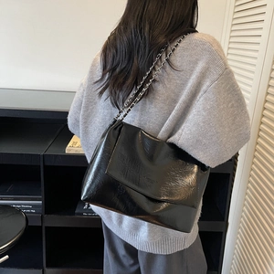 Minimalist black chain shoulder bag with glossy crinkled leather texture on model's shoulder