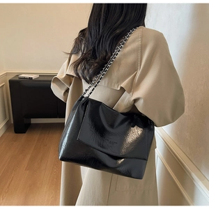 Detail of glossy black leather tote bag showing silver chain strap on model shoulder