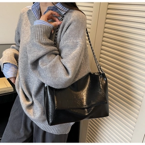 Detail of glossy black leather shoulder bag with leather-woven chain strap worn by model