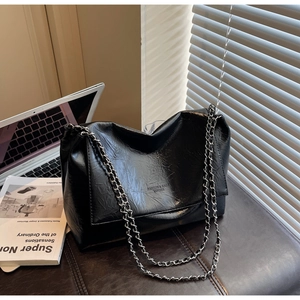 Close-up of black glossy chain shoulder bag on a desk with a laptop and magazines