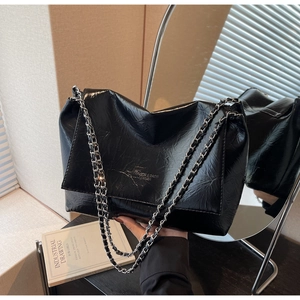 Detail of glossy pleated leather texture and silver chain strap on a black tote bag