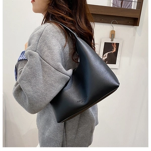 Detail of black leather hobo bag with Fashion and Bag Leather embossed text on gray outfit