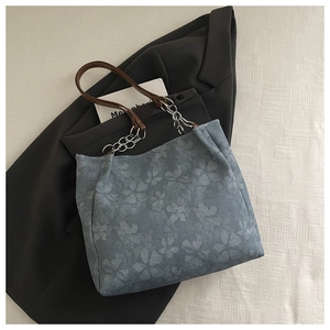 Detalle de bolso tote floral con correa de cuero marrón y cadena plateada