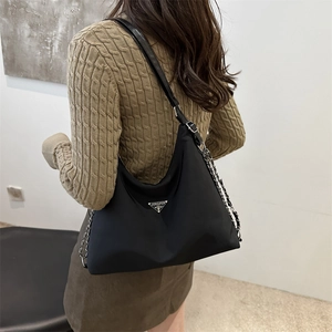 Minimalist black nylon shoulder bag with silver chain strap shown on model's shoulder