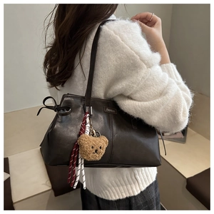 Detail of dark brown leather tote bag with metal logo, bow, and plush bear charm