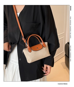 Détail d'un sac à bandoulière en nylon beige avec poignées et sangle en cuir orange