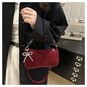 Detailed side view of a red crescent shoulder bag with silver chain and bow charm