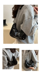 Close-up of black patent leather crescent bag with silver chain strap and metal stud base