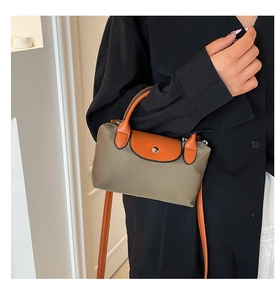 Détail d'un mini sac en nylon kaki avec rabat en cuir orange porté par un mannequin