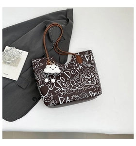 Dettaglio della borsa tote marrone scuro con motivi graffiti bianchi e ciondolo fluffy
