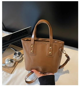 Detail of a brown leather mini tote bag with logo embossing and gold metal hardware
