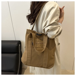 Détail du sac seau en toile marron montrant les poches zippées et la bandoulière réglable