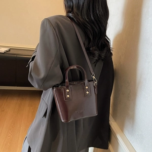 Sac seau chic en cuir brillant marron foncé avec poignée et ferrures dorées sur costume gris