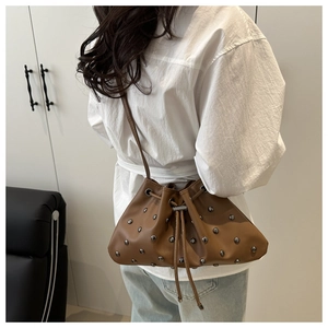Detail of brown leather drawstring bucket bag with silver studs and slim shoulder strap