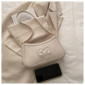 Detail of cream baguette bag with embossed G logo on soft faux leather texture