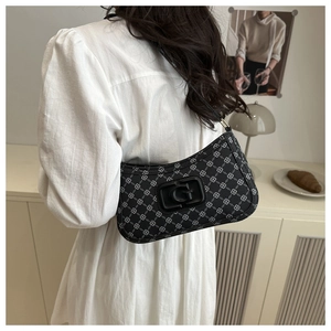 Detail view of black underarm bag featuring white floral patterns and G-letter plaque