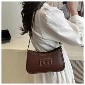 Detailed side view of brown leather shoulder bag with embossed G logo on a model